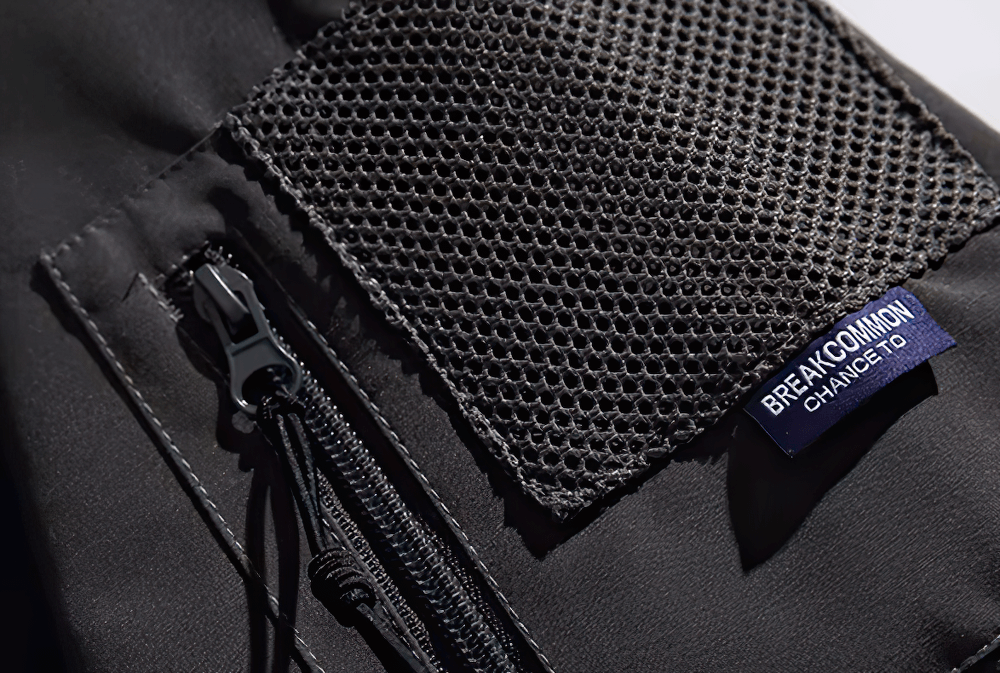 Close-up of black hiking jacket with zipper and mesh pocket, labeled 'Breakcommon' for urban and trail adventures.